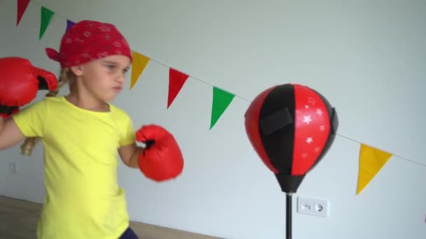 Kleines Mädchen in roten Boxhandschuhen, Boxsack. Gimbaler Bewegungsschuss. — Stockvideo