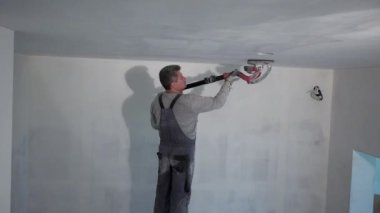 İnşaat işçisi zımparalama makinesiyle duvar yüzeyini düzleştiriyor