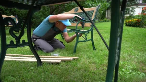 O tipo do carpinteiro desmonta o banco retro. Passos de renovação de mobiliário ao ar livre — Vídeo de Stock