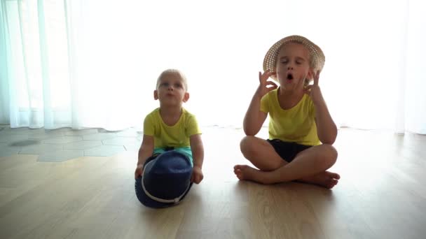 Смешные дети младшие брат и сестра делают вид, что занимаются йогой, сидя на полу — стоковое видео