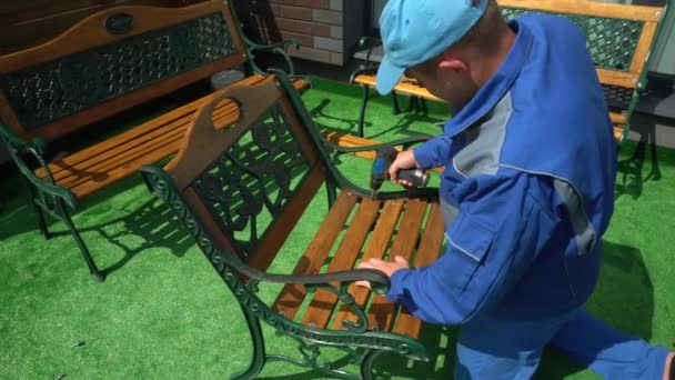 Homem com chave de fenda elétrica reparando cadeira de mobiliário ao ar livre no quintal da casa — Vídeo de Stock
