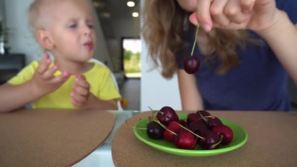 Fehér nő és szőke gyerek cseresznyeszedret eszik. sima kameramozgás — Stock videók
