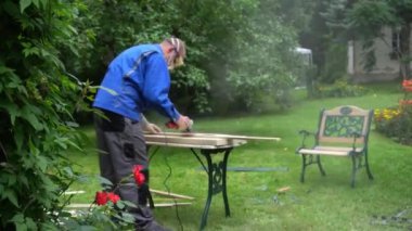 Sanding a wooden plank outdoors with orbital sander. Flowers and leaves
