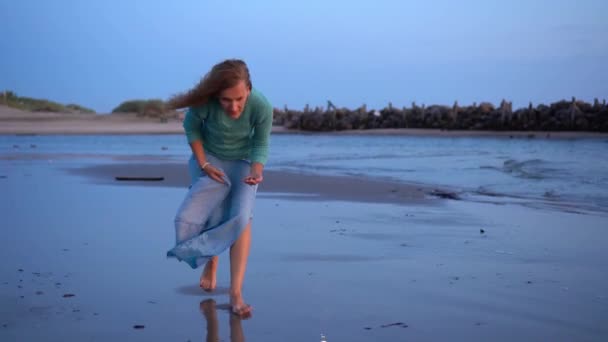 Woman collecting seashells on the beach and abandoned old pier or bridge. — ストック動画