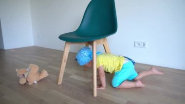 Little blond baby boy crawl under chair and play with teddy toy bear