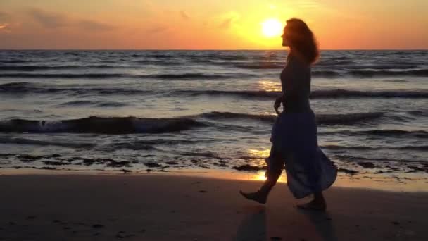 Silhouette of young woman in dress walking on the beach during sunset — 비디오