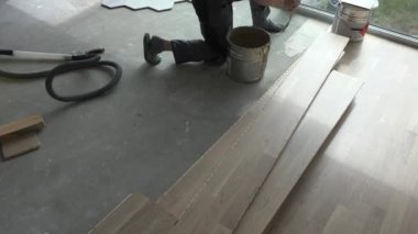 Unrecognizable worker apply glue on concrete floor. Oak floor board laying