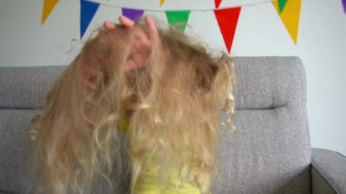 Komik küçük kız sarı saçlarla oynuyor ve kameraya gülümsüyor. Gimbal ağır çekim