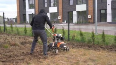 skilled worker man loosens soil with manual tractor in house yard. Gimbal shot