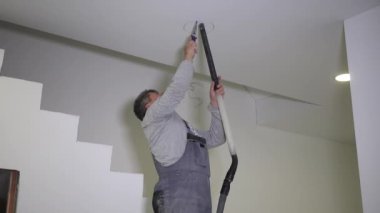 Electrician man with handsaw sawing hole in gypsum ceiling