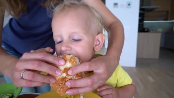 Madre alimentando a su hijo de 2 años con hamburguesa. Movimiento de cardán — Vídeos de Stock