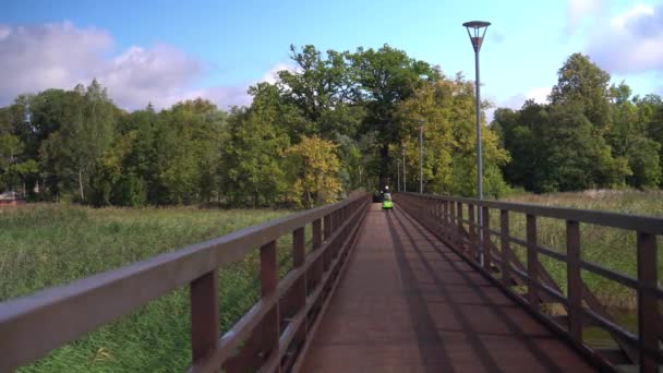 Unrecognizable senior man driving small scooter through wooden footbridge — Stock Video