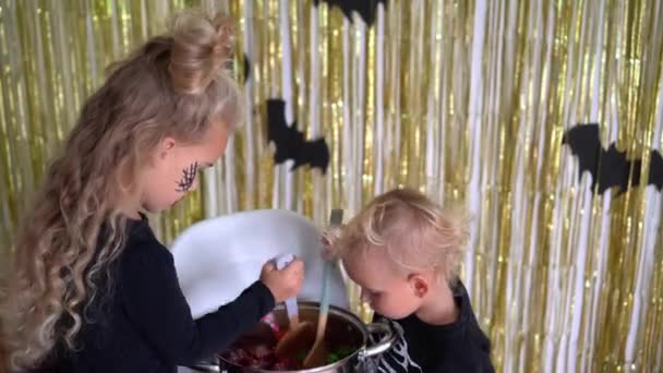 Witch blond sister and little skeleton brother baking sweets in big pot — Stockvideo