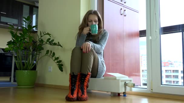 Mujer solitaria sentarse en el radiador y beber té caliente . — Vídeos de Stock
