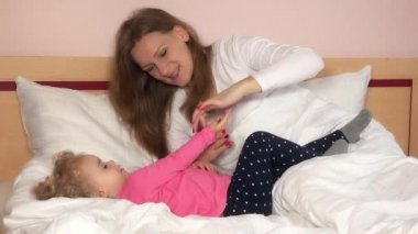 Anne kızıyla oynuyor, ellerini gıdıklıyor ve yatak odasında gülüyor. 4k