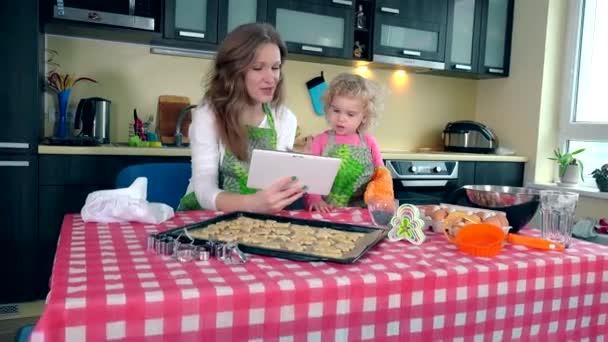 Mother with little daughter looking for recipe on tablet in kitchen. 4K — Stock video