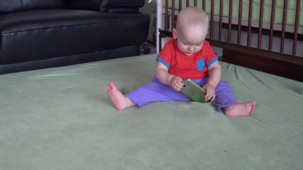 Adorable niño pequeño sentarse en la sala de estar y jugar con el teléfono inteligente — Vídeos de Stock