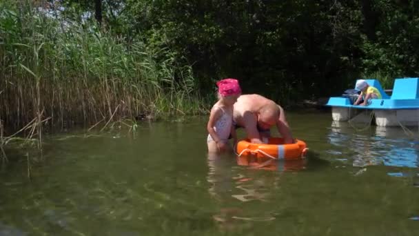 Papa leert dochter zwemmen met een reddingsboei. Zoon op catamaran. Gimbal motie — Stockvideo
