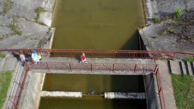 Aile terk edilmiş eski baraj köprüsünde yürüyor. Yetişkinler ve çocuklar seyahat eder.