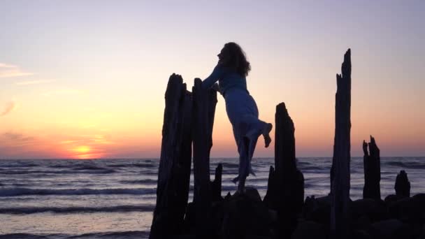 Романтичная женщина позирует на старом морском пирсе и лесах на оранжевом закате — стоковое видео