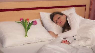 Genç bir kadın uyanıyor ve beyaz yastıkta üç lale buluyor. 4k