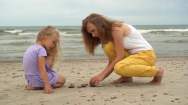 Anne, deniz kıyısında çakıl taşları taşıyan 5 yaşında bir kız çocuğu..