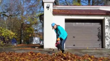 Sonbaharda garaj girişinden yaprakları temizleyen kadın işçi.