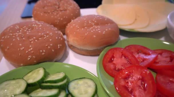 Gurka tomater bulle och ost nära kokplatta med bakning köttbullar för burgare — Stockvideo