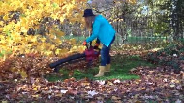 Yaprak üfleyicisi olan kız sonbahar bahçesinde güzel lale ağacının altında yaprak üflüyor..