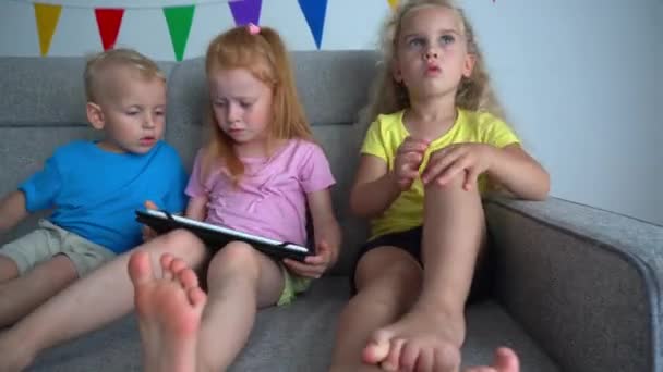 Crianças discutindo para jogar com tablet digital em um sofá. Amigos viciados — Vídeo de Stock