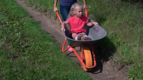Happy mother driving a wheelbarrow, while her preschooler daughter riding in it — Stock Video