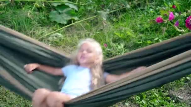Aktives kaukasisches kleines Mädchen schwingt in Hängematte, die an Gartenbäumen hängt — Stockvideo