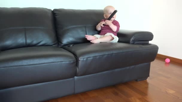 小男孩坐在沙发上看电视，玩遥控器 — 图库视频影像