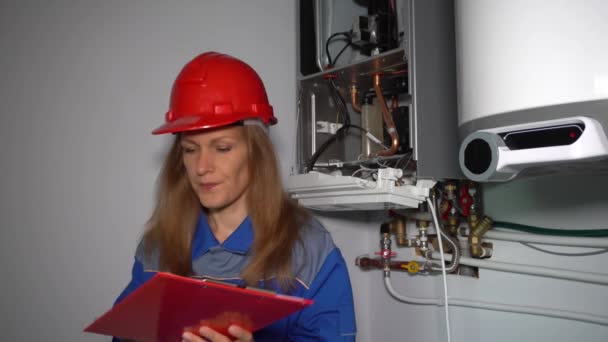 헬멧을 쓰고 난방 장치의 기술 데이터를 확인하는 진지 한 기술자 여자 — 비디오