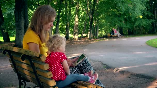 Мати і дівчина використовують планшет, сидячи на лавці в парку. сучасна освіта. 4-кілометровий — стокове відео