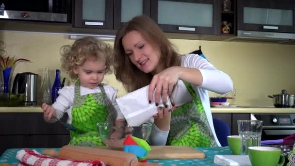 Vrouw giet chocolade bloem in glazen schaal en kind meisje meng het met lepel — Stockvideo