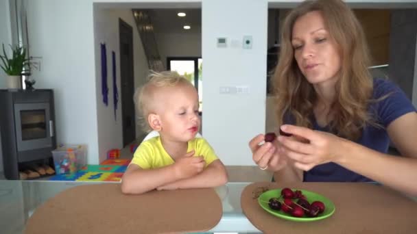 Múmia adorável alimentando seu filho com cereja em casa. Mãe beijando filho — Vídeo de Stock