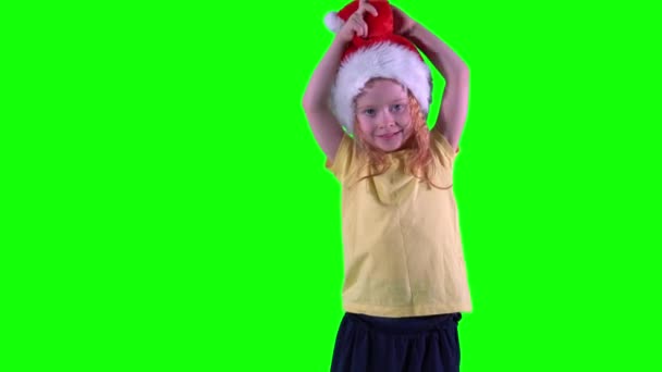 Забавная рыжая девчонка играет с рождественской шляпой. Зеленый фон ключа хромы — стоковое видео
