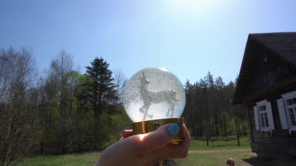 Рука держит игрушку в форме единорога в шаре с искусственным снегом на голубом небе — стоковое видео