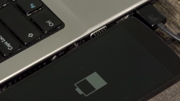Статус зарядки батареи смартфона на экране рядом с ноутбуком — стоковое видео