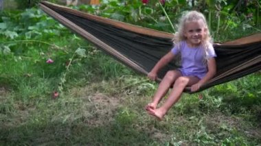 Mutlu küçük kız yaz bahçesinde bir hamakta oturuyor.