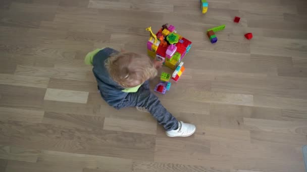 Vier jaar oude jongen speelt speelgoed blokken op de vloer. Gimbal beweging close-up bovenste schot — Stockvideo