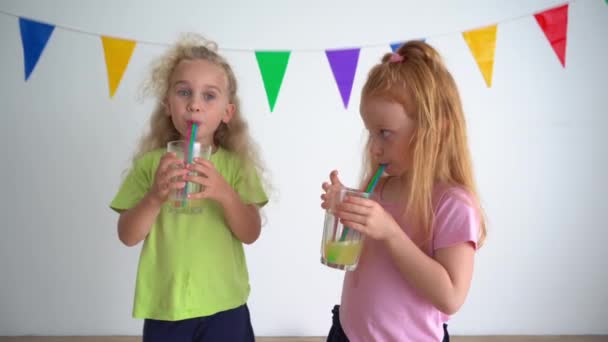 Dos niñas están bebiendo jugo de naranja de un vaso usando paja — Vídeo de stock