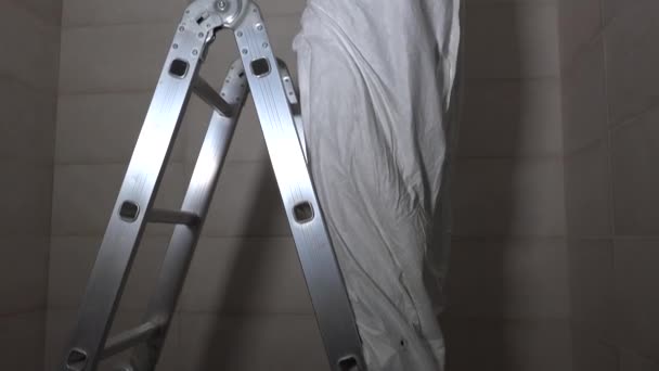 전기 기술자는 사다리에 서서 납 램프의 천장에 구멍을 뚫습니다. 4K — 비디오