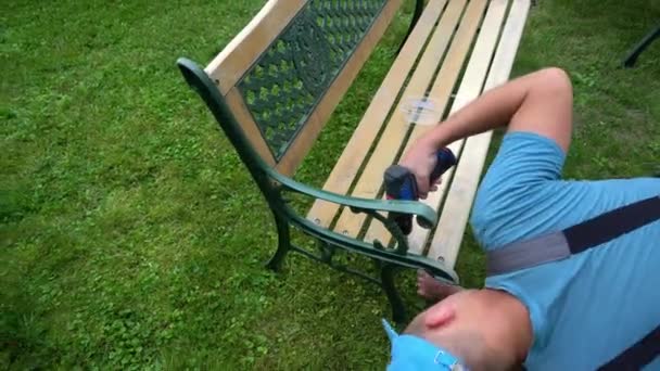 Carpinteiro homem desenroscar parafusos de banco retro. Processo de renovação de mobiliário de exterior — Vídeo de Stock