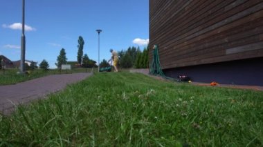 Çimleri biçen genç adam. İşçi arka bahçede işini yapıyor. Gimbal hareketi