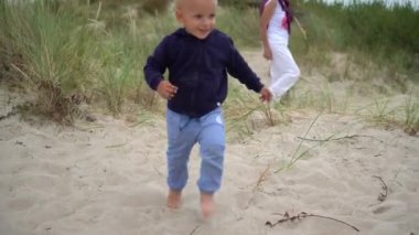 Sevimli küçük çocuk kum tepeciklerinin arasından annesine ve kardeşine doğru koşuyor.