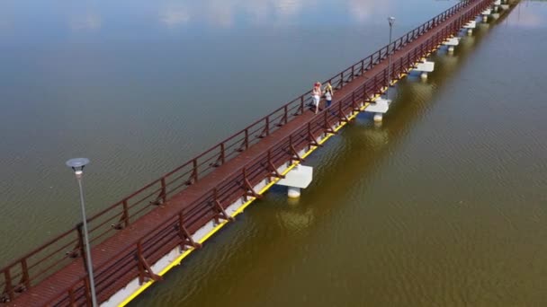 Hombre y mujer llevan a sus hijos en la cabeza caminando por el puente a través del lago — Vídeo de stock