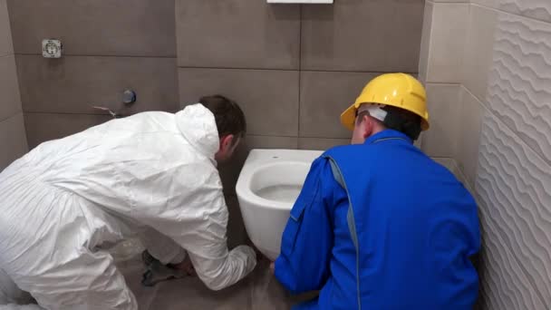 Dois homens encanador pendurado vaso sanitário pesado pan no novo banheiro moderno — Vídeo de Stock