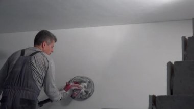 Marangoz yeni apartman duvarında elektrikli zımpara makinesi kullanarak zaman kazanıyor.